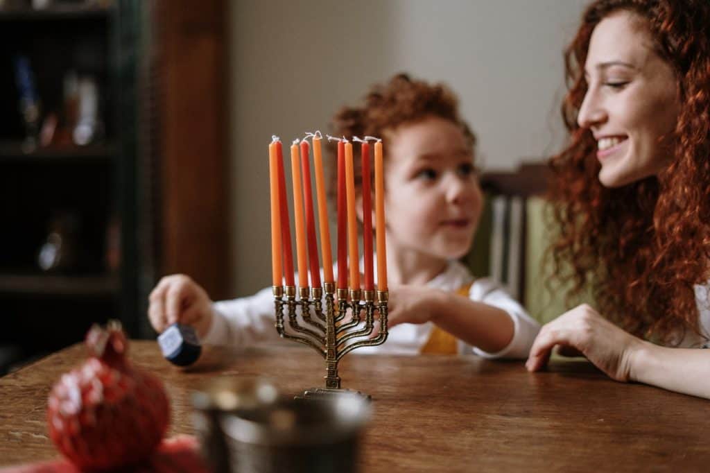 אמא וילד יושבים מול חנוכיה עם 8 נרות וסביבון